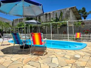 three chairs and an umbrella next to a swimming pool at Casa das Flores com piscina in Matinhos