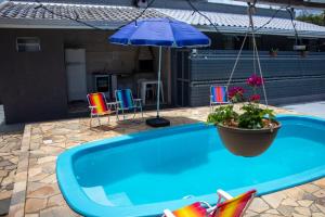 a blue pool with a potted plant and an umbrella at Casa das Flores com piscina in Matinhos
