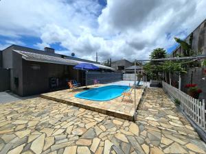 a swimming pool in a yard with a stone patio at Casa das Flores com piscina in Matinhos