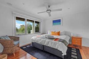 a bedroom with a bed and a chair and windows at Surfbreak, Culburra Beach in Culburra Beach