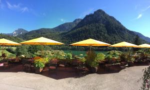 a group of tables with yellow umbrellas in front of a lake at Hotel Pension Hubertus in Bad Reichenhall