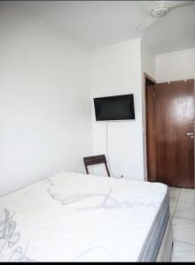Un dormitorio con una cama y un televisor en una pared. en Apartamento Mirim Praia Grande, en Praia Grande