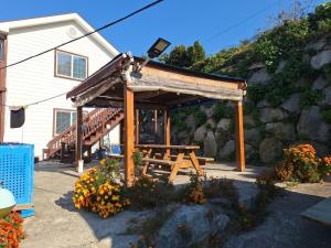 a wooden picnic shelter with a bench in front of a house at Yeosu Geumodo Badaae Pension in Yeosu