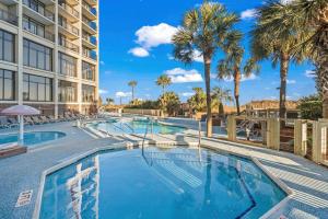 a swimming pool with palm trees and a building at Ocean Front at Beach Cove in Myrtle Beach