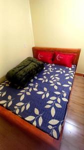 a bed with a blue comforter and two red pillows at Homestay Quyền Linh-Tour Tây Côn Lĩnh in Kon Rung (1)