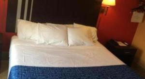 uma cama com lençóis brancos e almofadas num quarto de hotel em Travelodge by Wyndham Bay Shore Long Island em Bay Shore