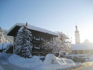 a building covered in snow with a clock tower in the background at Gasthof-Pension Golob in Kirchbach