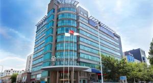 青岛Jinjiang Metropolo Hotel - Qingdao Chengyang District Government的前面有旗帜的高大的玻璃建筑