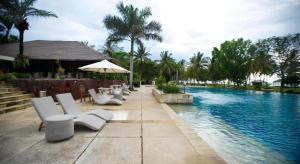 a swimming pool with white chairs and an umbrella at Tanjung Lesung Beach Hotel in Kalicaah
