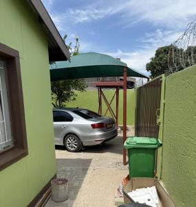 卡蒂马穆利洛Namasiku's Self Catering的一辆车停在一栋绿色建筑旁边，旁边撑着一把绿色的伞。