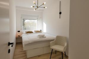 a white bedroom with a bed and a chair at Apartments Lia in Ljubljana