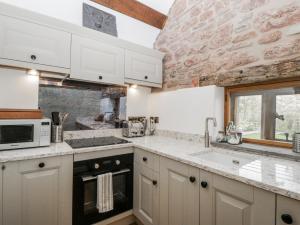 a kitchen with white cabinets and a stone wall at Walnut Cottage in Usk