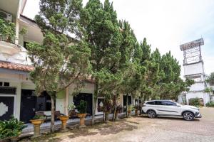 Un coche aparcado delante de un edificio con árboles. en New Abadi Hotel Tasikmalaya, en Tasikmalaya