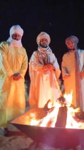 a group of three men standing around a campfire at Tenere Luxury Camp in Merzouga