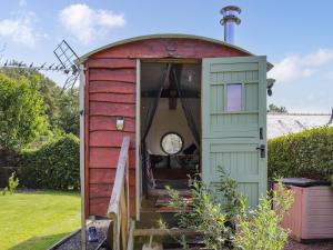 un piccolo capanno rosso con un orologio sulla porta di Glan Tywyn Shepherds Hut a Caeʼr-geiliog
