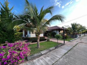 a palm tree in front of a house with flowers at Himnam Phusang Resort in Ban Pa Sak