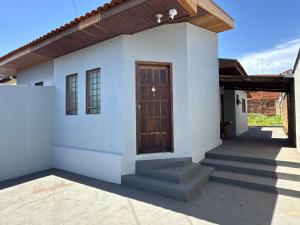 a small white house with a wooden door at Casa completa, ar e vaga, perto parque Ecológico in Ourinhos