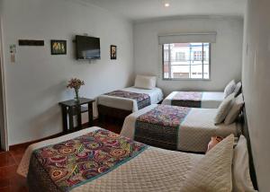 a hotel room with three beds and a tv at Hotel Villa Karina in Bogotá