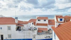 een groep gebouwen met rode daken en de oceaan bij Fonte do Norte in Ericeira