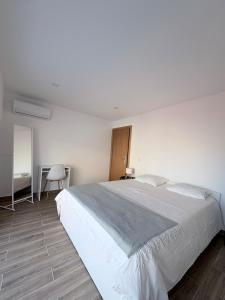 a white bedroom with a large bed and a chair at Figueira Guesthouse in Figueira da Foz