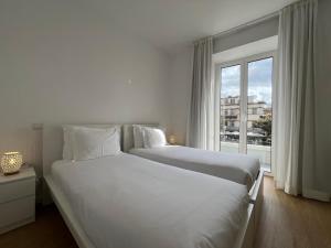 a white bedroom with two beds and a window at Market Downtown T3 in Funchal