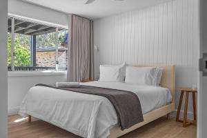 a bedroom with a bed with white sheets and a window at Luna Beach House, Vincentia in Vincentia