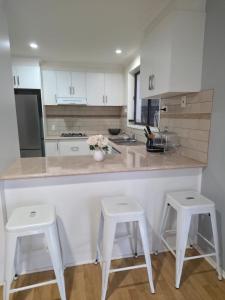 a kitchen with white cabinets and two white stools at 4 Westcott Parade Rockbank in Rockbank