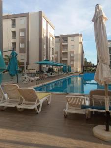 a pool with chairs and umbrellas next to a hotel at Appartement Neuf au Bord de la Mer - Hammamet Sud Zone Touristique in Hammamet