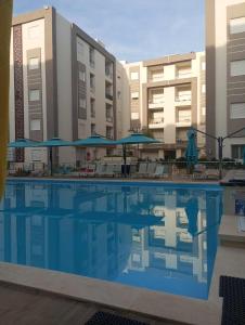 a swimming pool with chairs and umbrellas in front of buildings at Appartement Neuf au Bord de la Mer - Hammamet Sud Zone Touristique in Hammamet
