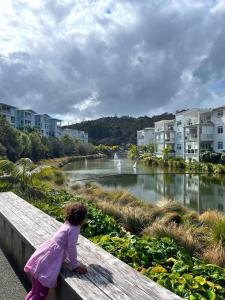 Ein kleines Mädchen sitzt auf einer Bank und schaut auf einen Fluss. in der Unterkunft Five Olives Holiday House - 350m to beach in Orewa + 13 Fotos