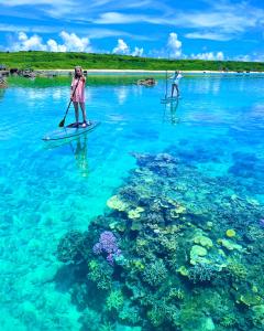 two people on paddle boards in the water with reefs at 無料レンタカー付 ReHaQ宮古島バケーションレンタルハウス in Miyako Island