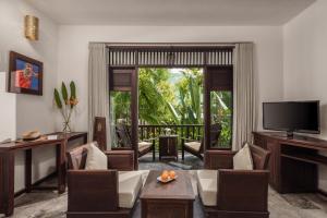 a living room with a television and a couch and chairs at Legacy Hoi An Resort in Hoi An