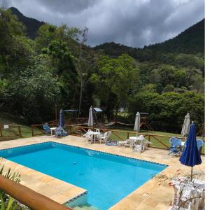 a swimming pool with chairs and umbrellas next to a mountain at Chalé com vista deslumbrante in Teresópolis