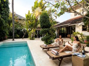 zwei Frauen sitzen auf Stühlen neben einem Swimmingpool in der Unterkunft Villa White Orchid Seminyak in Seminyak