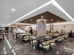 鄂尔多斯Venus Royal Hotel Ordos Yijinhuoluo Banner Olympic的一名男子站在摆着桌椅的餐厅里
