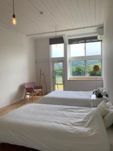 a bedroom with two beds and a chair and two windows at 里山のいぶき舎 in Goto