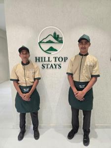 Dos hombres uniformados de pie frente a un cartel que dice "Quedarse en la cima de una colina" en Hill Top Stays, en Navi Mumbai