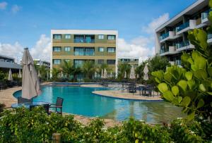 a swimming pool with tables and umbrellas in front of a building at Mana Beach Experience Muro Alto C219 in Porto De Galinhas
