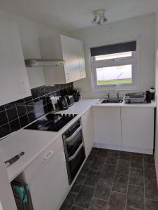 eine Küche mit weißen Schränken und einer Spüle und einem Fenster in der Unterkunft Antonia's Place 337 California Sands in Scratby