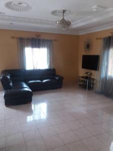 Jeng's paradaise green house في Sukuta: غرفة معيشة مع أريكة جلدية سوداء وتلفزيون