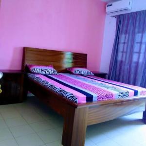 een groot houten bed in een kamer met roze muren bij Chez Amina in Mbour