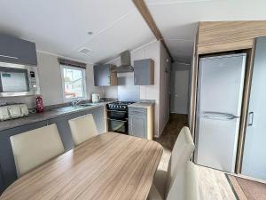 内兹岬附近沃尔顿Lovely 8 Berth Caravan With Decking To Hire At Naze Marine In Essex Ref 17030Ga的一间带木桌的厨房和一间带冰箱的厨房