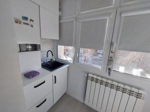 a kitchen with white cabinets and a sink and two windows at Spania Studio in Craiova