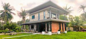 他朗Leamsai Whisper Home的一栋带阳台的房子，坐落在绿草茵茵、棕榈树环绕的草坪上。