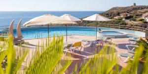 a swimming pool with chairs and umbrellas and the ocean at Zeeva Hotel and Resort in Torre Dei Corsari