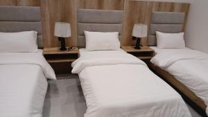 Tres camas en una habitación con sábanas blancas y lámparas. en W Hotel Apartment, en Taif 1 foto más