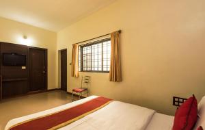 a bedroom with a bed and a window and a television at Super Hotel O Sai Kalyan Suites in Chikmagalūr