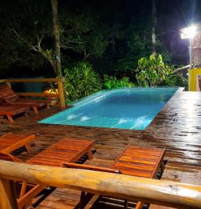 ein Schwimmbad bei Nacht mit Holztischen und Stühlen in der Unterkunft Odoya Morro de São Paulo in Morro de São Paulo