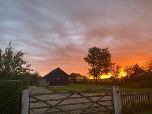 a fence and a barn with a sunset in the background at Rhubarb Barn bedroom only in Diss +8 photos