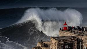 a large wave is crashing on a pier with a lighthouse at Océane Guest House - Adults only in Nazaré